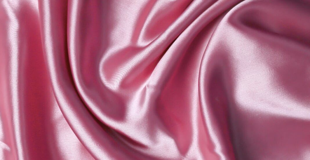 Shiny pink polyester spandex fabric with smooth, flowing folds, reflecting light.