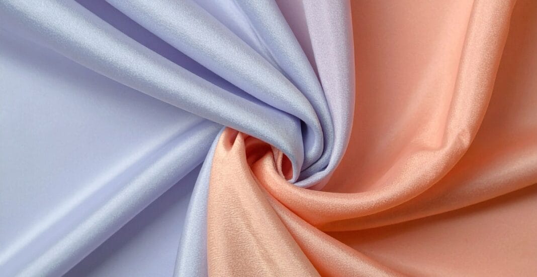 Close-up of pastel-colored chiffon fabric in lavender and peach, gently gathered and twisted to showcase its silky texture.