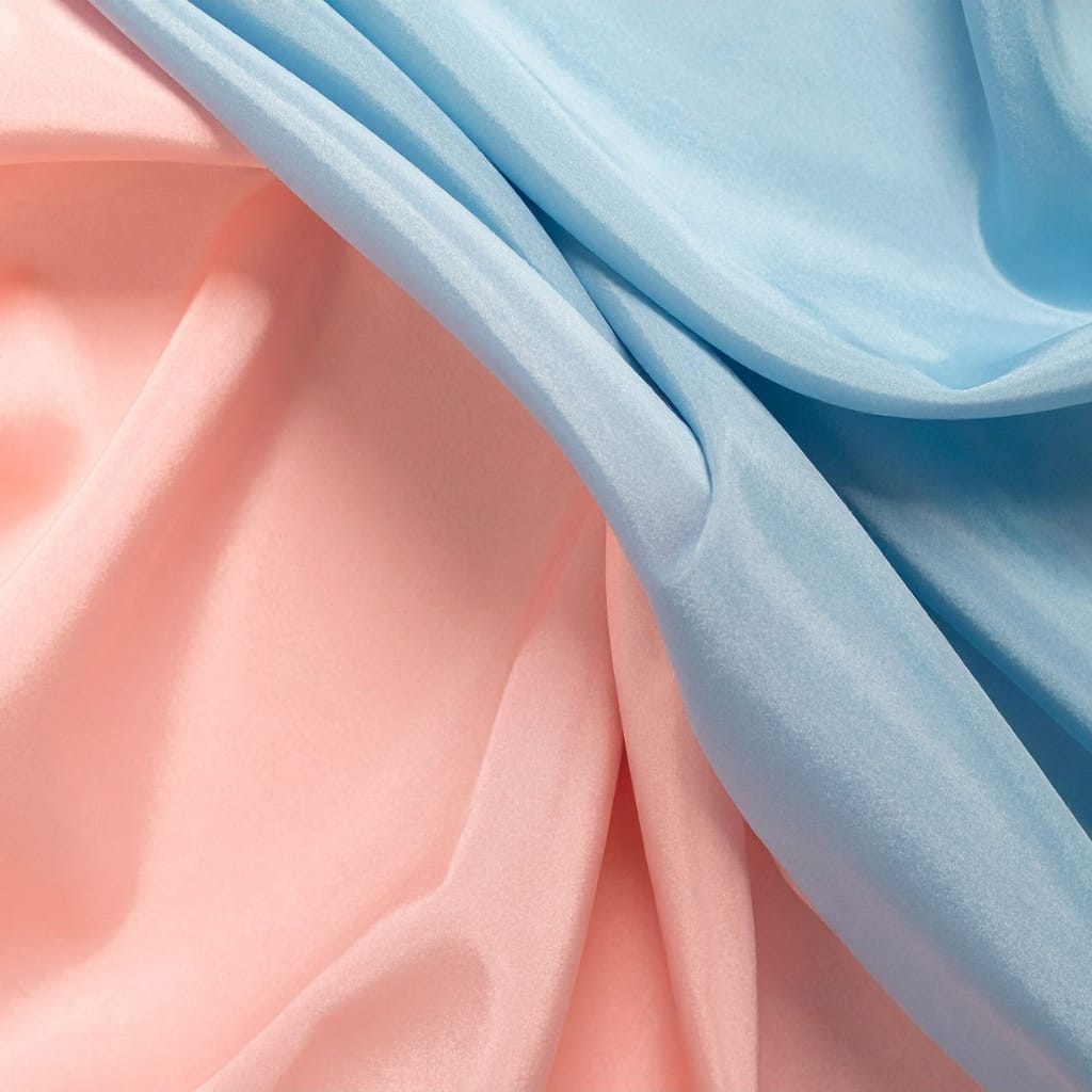 Close-up image of smooth, soft satin chiffon fabric in pastel pink and blue, softly draped to showcase its sheen and delicate texture.