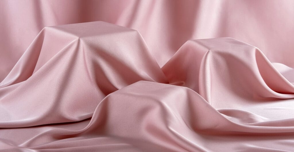 Close-up of pink satin fabric draped softly, showcasing its smooth and shiny surface with flowing folds.