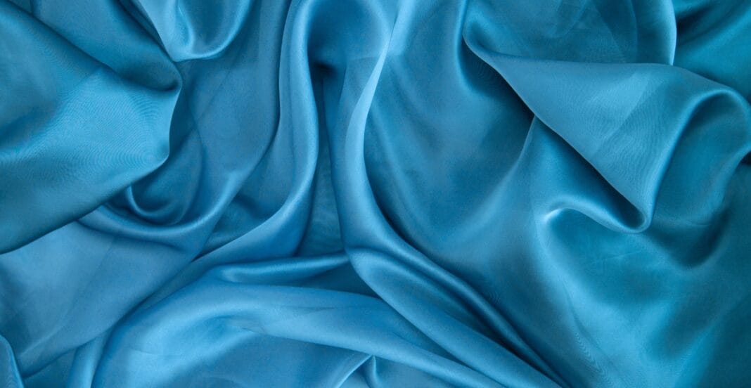 Close-up image of flowing blue satin organza fabric with gentle folds and a smooth, shiny surface.