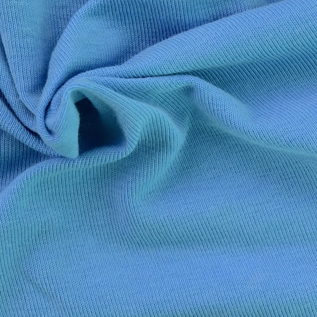 Close-up image of a light blue, textured fabric with soft folds, showcasing fine, closely woven threads.