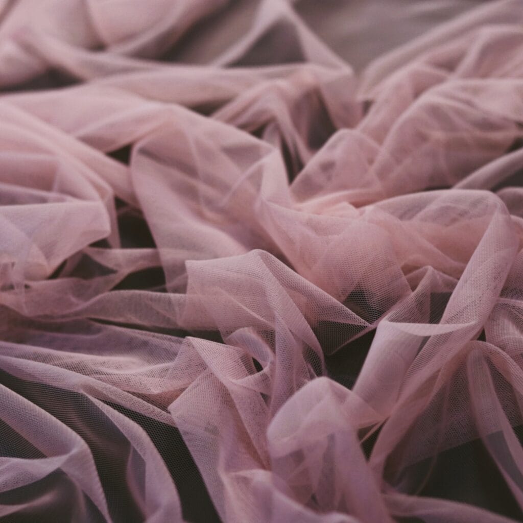 A close-up view of soft, pink, sheer fabric ruffles with a delicate and flowing texture.