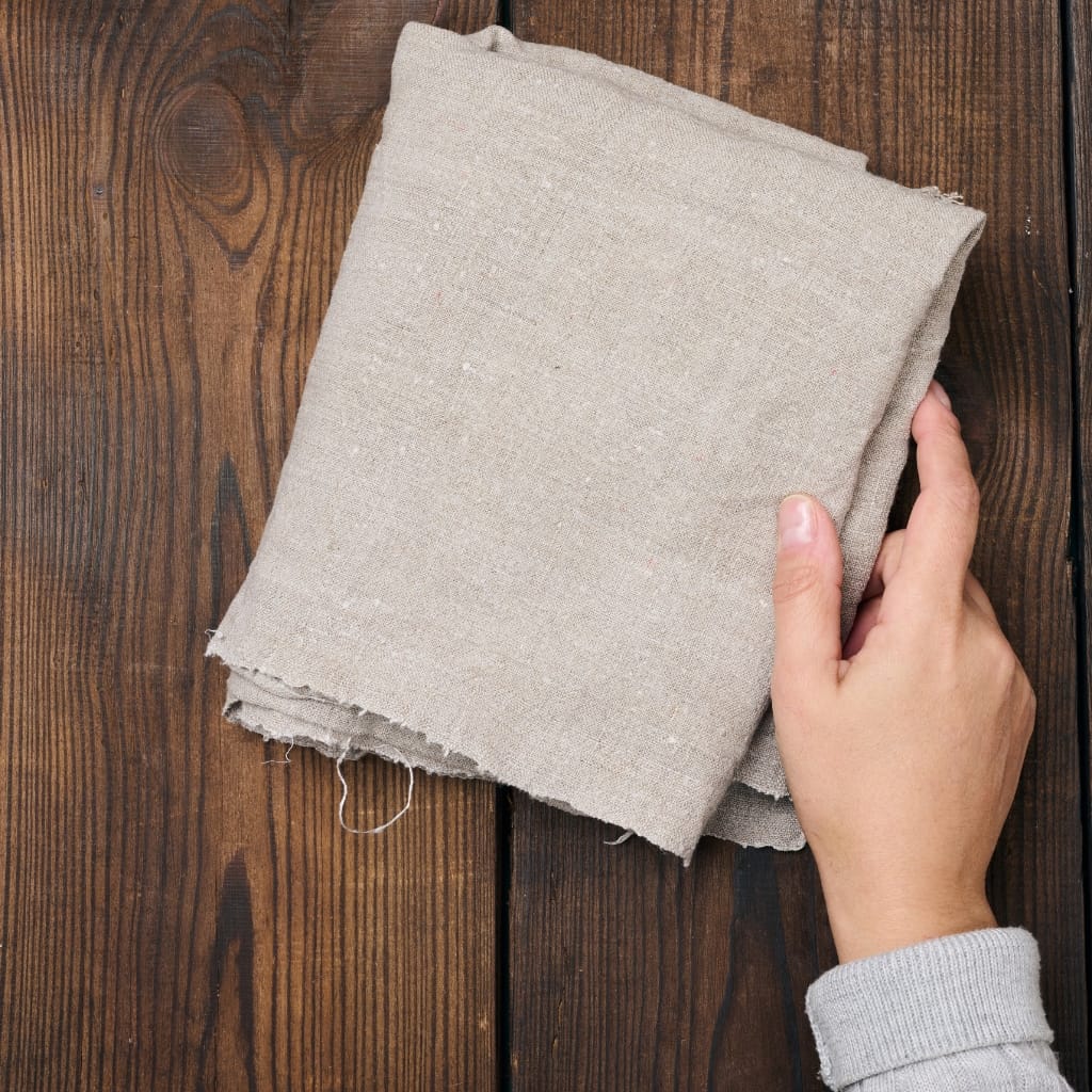 A person's hand holding a folded piece of beige fabric over a wooden surface.
