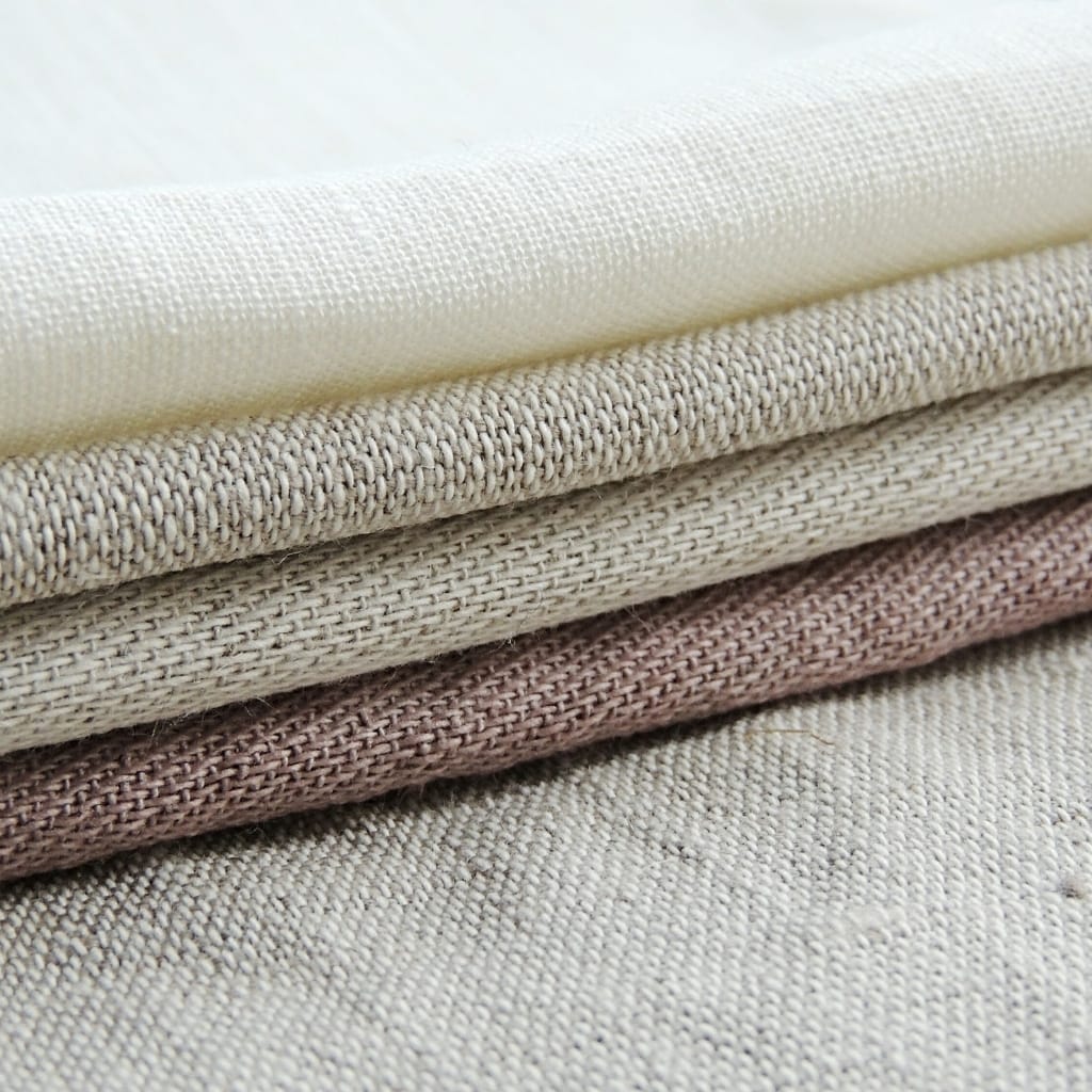 A close-up shot of stacked, folded fabrics in neutral shades, showcasing textured weaves and natural finishes.