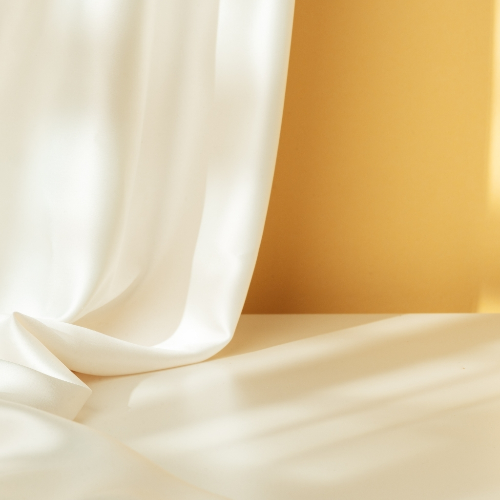 Close-up of elegant cream-colored satin fabric with gentle folds and a soft background wall.