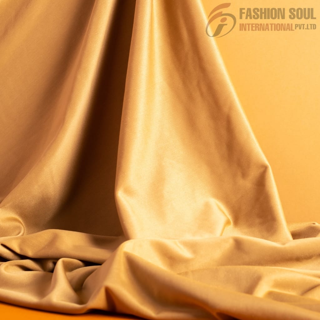 A close-up of shiny, smooth fabric in a golden color, draped with elegant folds. The fabric is silky and reflective, giving it a luxurious appearance.
