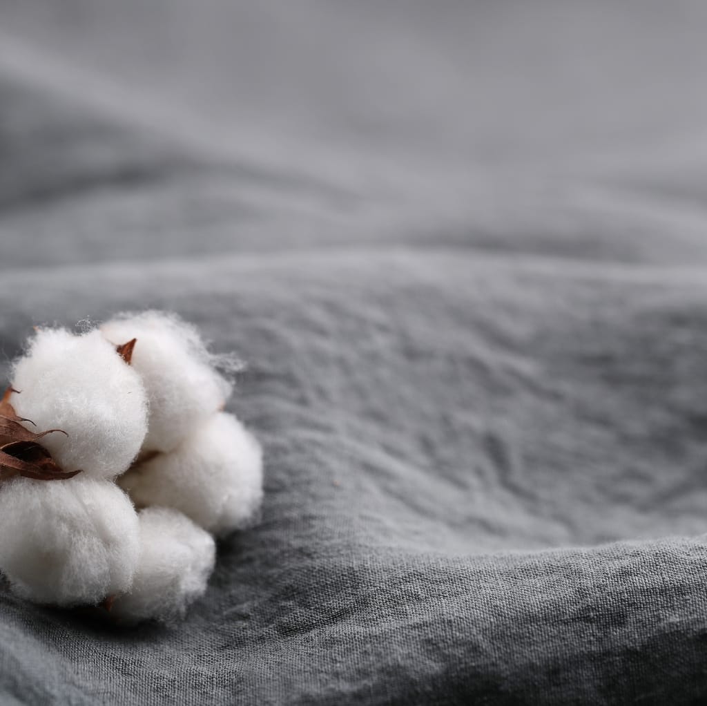 Close-up image of soft, white cotton bolls resting on a gray fabric surface, highlighting the natural texture and fiber of raw cotton.