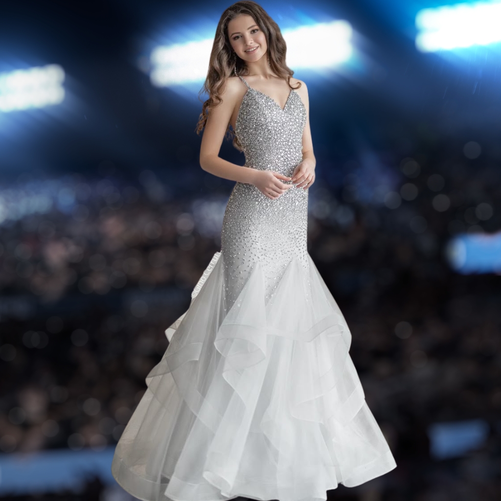 A young woman wearing a stunning tulle mermaid dress with a sparkly, embellished bodice, standing against a blurred, dark background with bright lights.