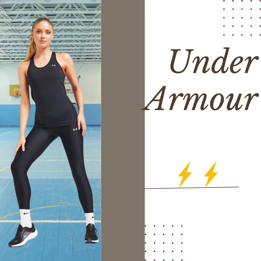 A woman in a black Under Armour sports outfit, including a sleeveless top, leggings, and sneakers, standing in a gymnasium with a basketball court in the background.