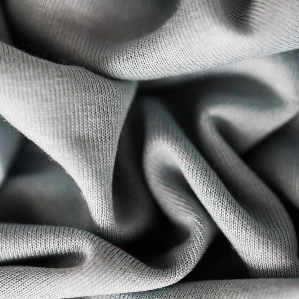 Close-up image of soft, textured gray cotton fabric with gentle folds and intricate weave patterns.