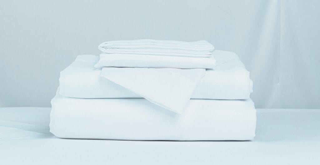 A neatly folded stack of white bed linens on a light blue background.