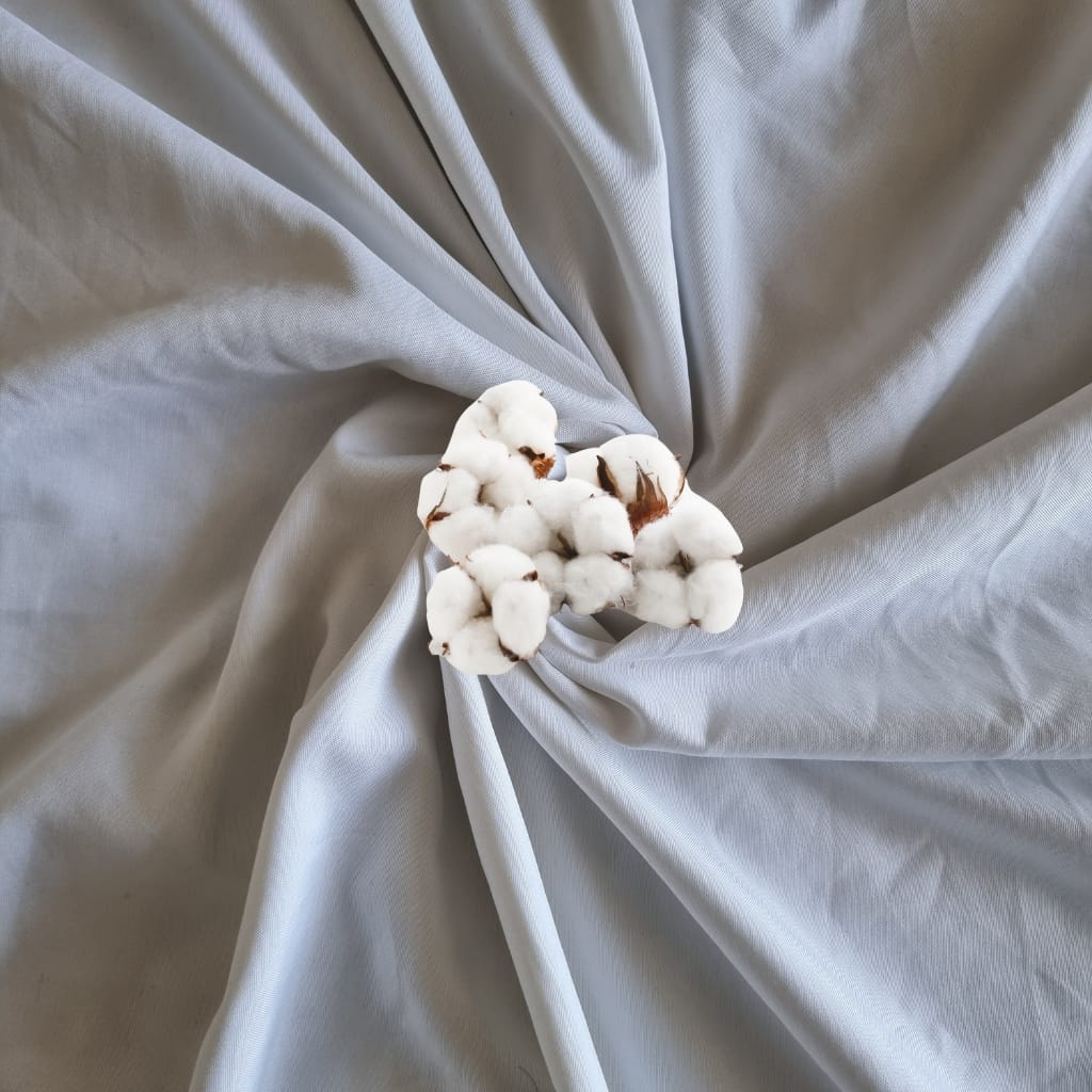 A small cluster of cotton bolls resting on a light grey, slightly wrinkled fabric background.
