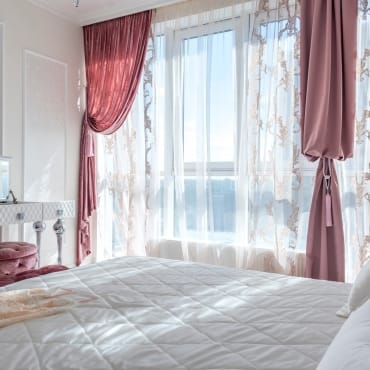 Soft pink velvet curtains framing a large window with sheer floral curtains, creating an elegant and cozy bedroom setting.
