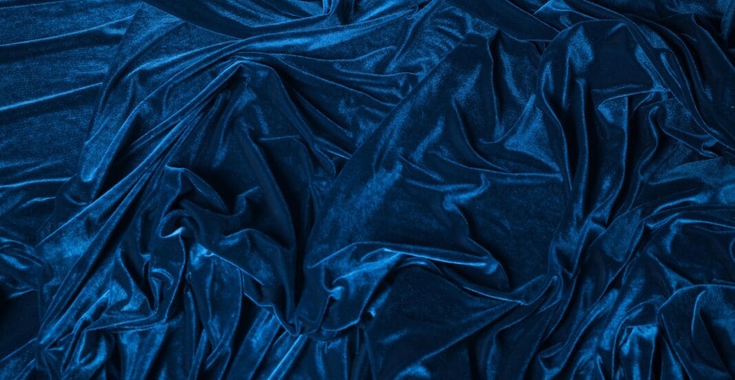 Close-up image of deep blue velvet fabric with soft, luxurious folds and a shiny, plush surface.