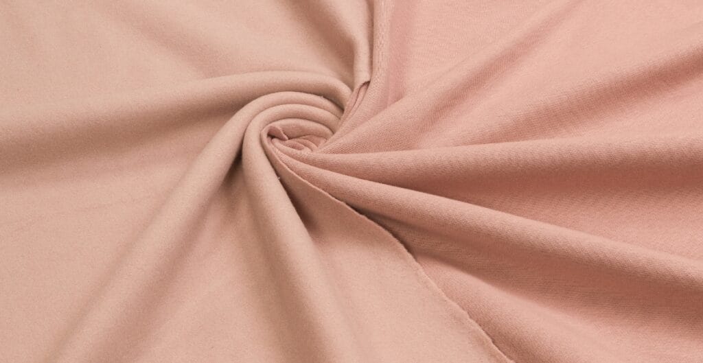 A close-up view of soft, pink cotton spandex fabric twisted into a spiral, showcasing its smooth texture and slight stretch.