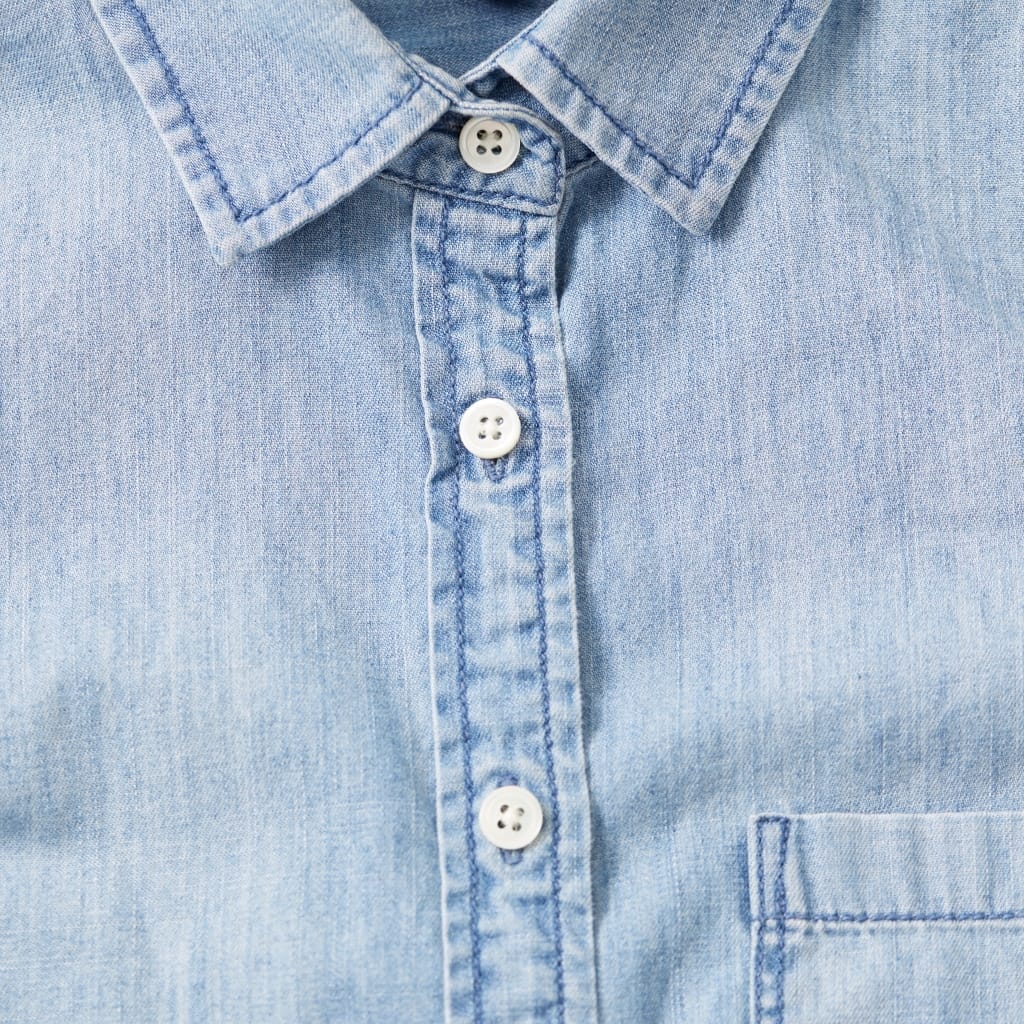 Close-up of a light blue chambray shirt with a button-down collar, showing the fabric texture and buttons.