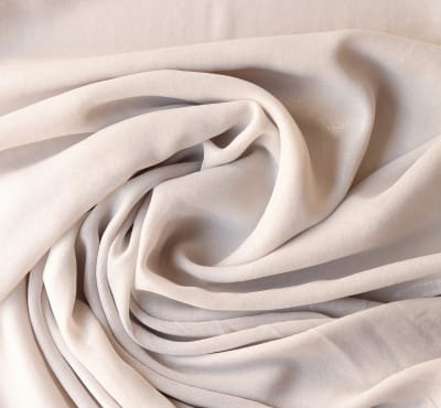 A close-up image of soft, flowing, cream-colored fabric with a smooth and slightly shiny surface, showcasing the luxurious texture of cotton-silk fabric.