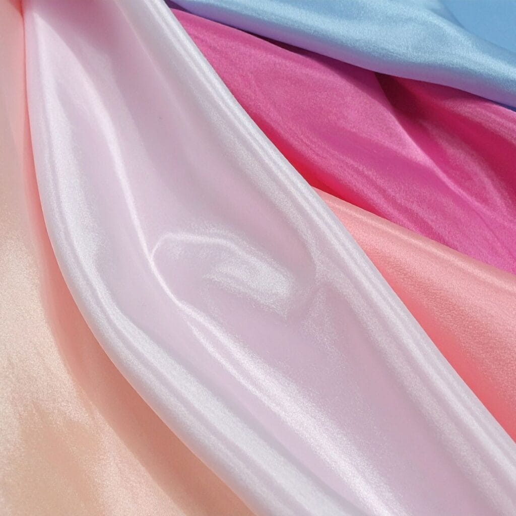 Close-up of overlapping pastel-colored satin fabric in shades of pink, lavender, and blue, showcasing their shiny texture and soft folds.