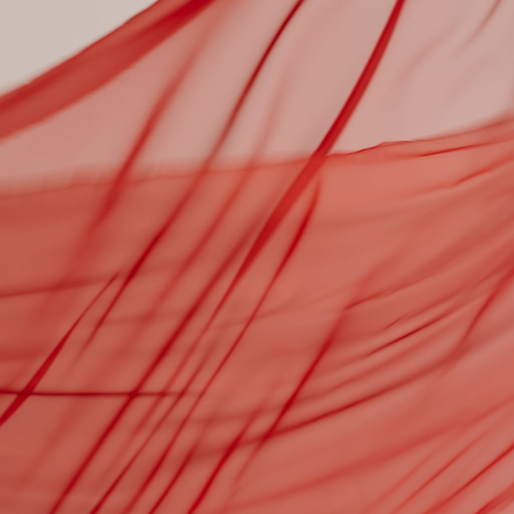 Close-up image of crystal organza fabric showing its lightweight, sheer, and crisp texture with fine red lines running through its transparent surface. The fabric appears slightly crinkled, enhancing its textured appearance.