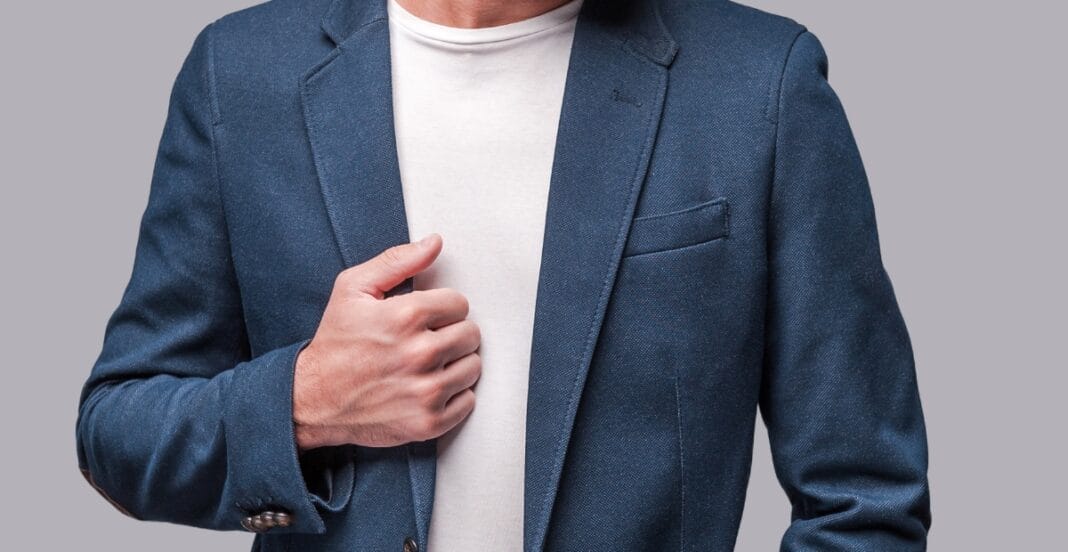 Close-up of a person wearing a blue blazer over a white t-shirt, with their hand adjusting the jacket.