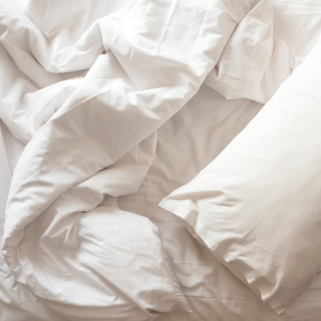A close-up of crumpled white bedsheets and pillows, creating a soft, inviting, and cozy appearance.