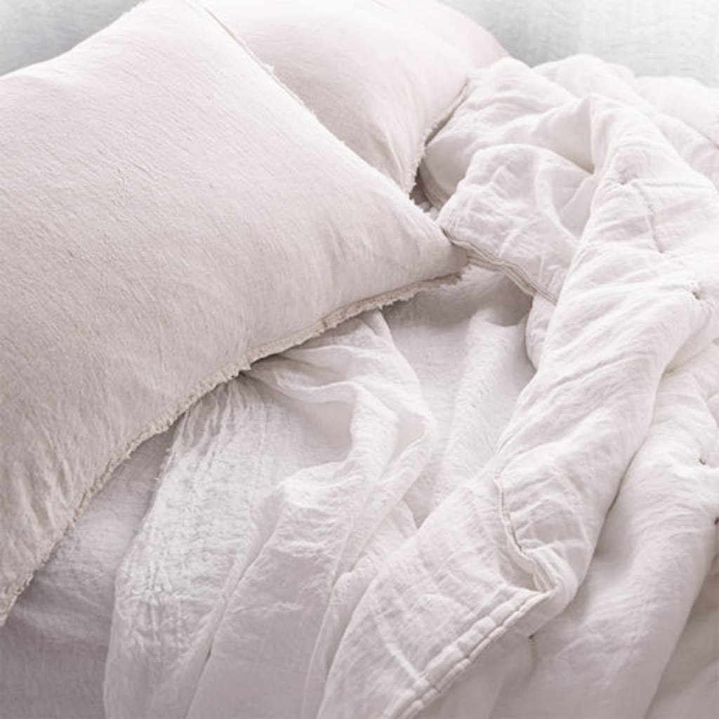 A close-up view of a neatly made bed with soft, white linens and fluffy pillows, featuring a cozy and inviting appearance.