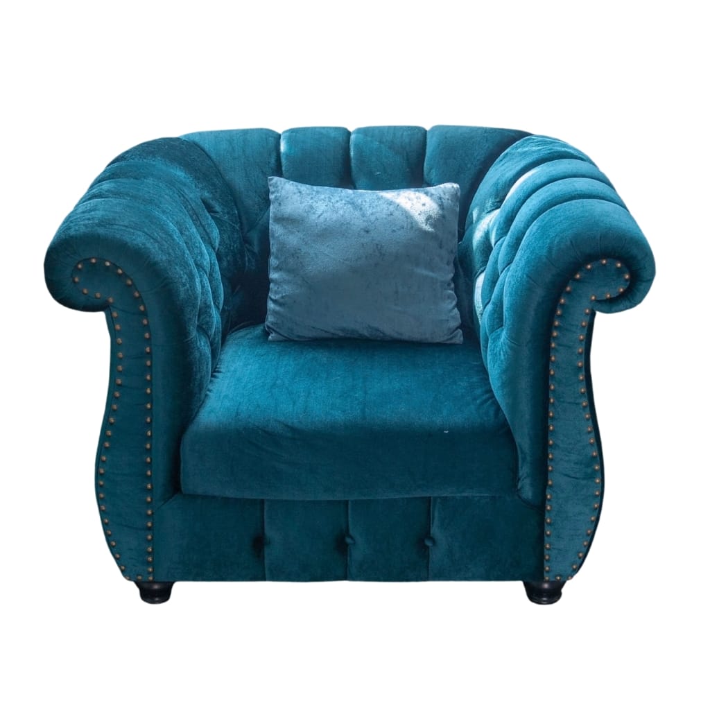 A luxurious, tufted velvet armchair in a rich teal color with rolled arms and decorative brass nailhead trim, set against a plain white background.