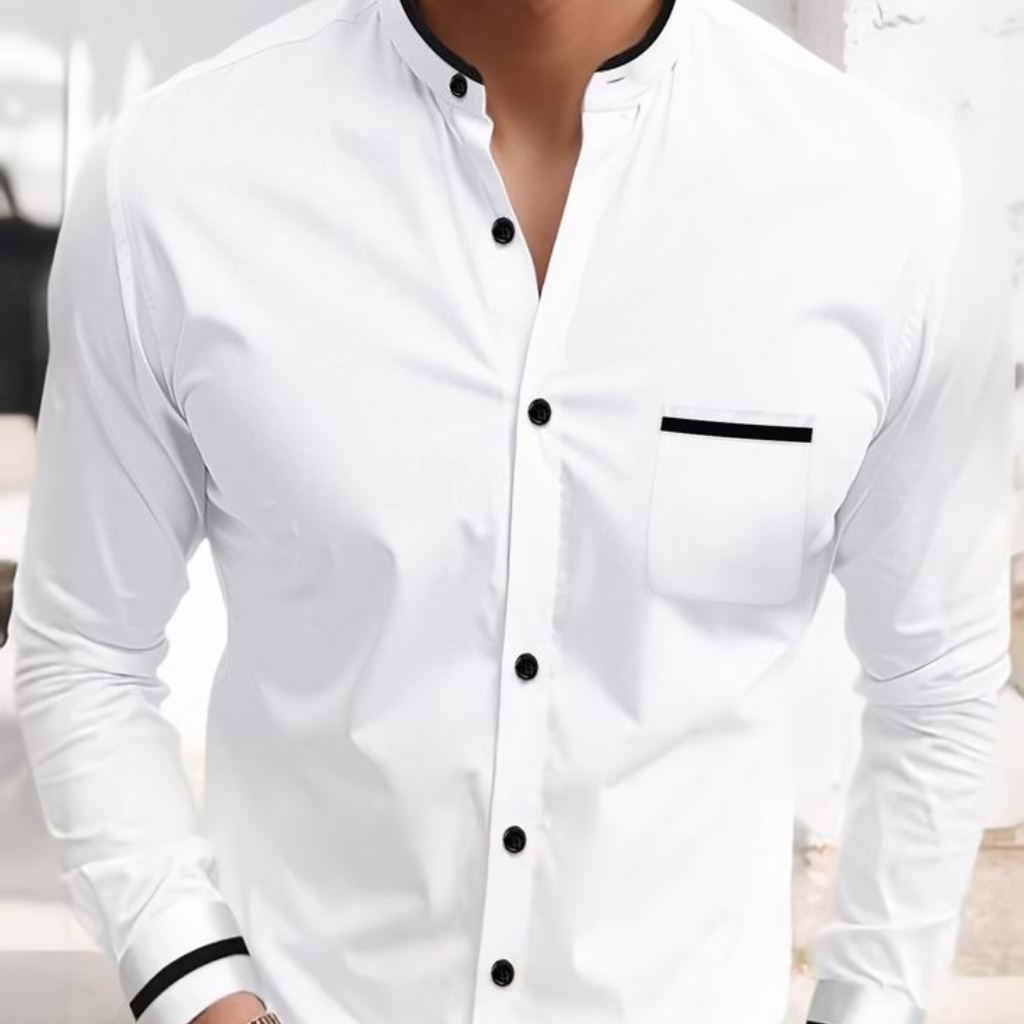 A close-up image of a white cotton button-down shirt with black accents on the collar, buttons, pocket trim, and cuffs, worn by a person with hands on hips.