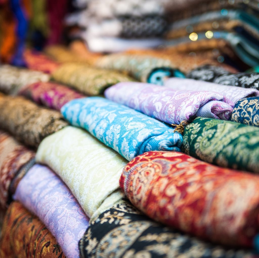 A vibrant display of colorful, intricately patterned fabrics rolled and stacked, showcasing various textures and designs.