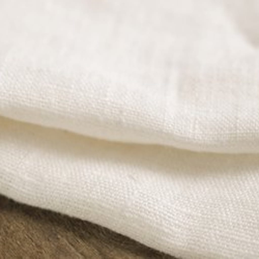 Close-up of soft, white fabric with a textured, woven surface, draped over a wooden surface.