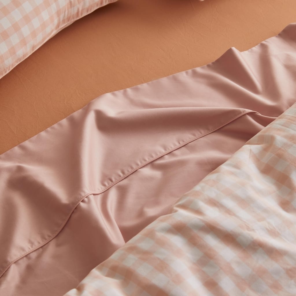 Close-up of a bed with peach-colored sheets, featuring a satin pillowcase and a checkered pillowcase in soft pastel shades, against a peach-colored bedspread.