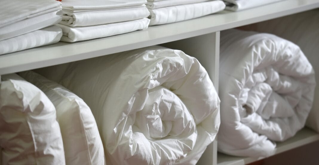 Shelves with neatly rolled white comforters and folded linens.