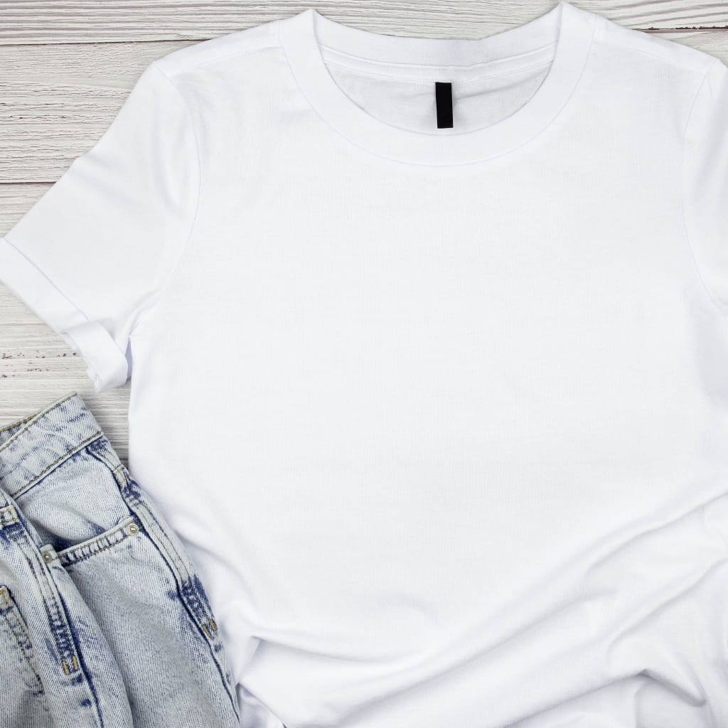 A plain white T-shirt laid flat on a light wooden surface, partially overlapping a pair of light blue denim jeans.