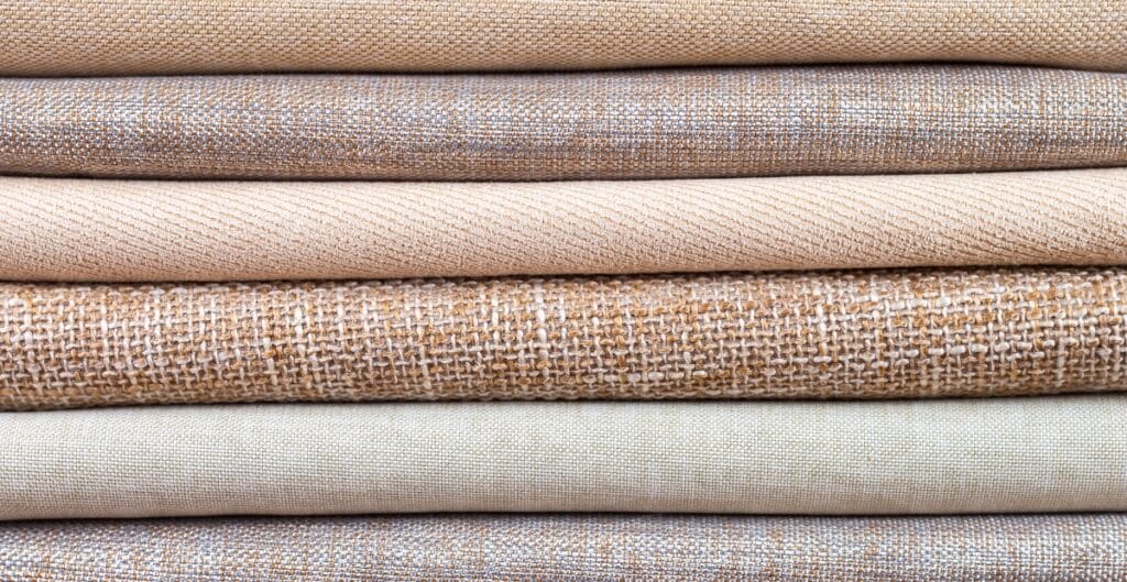 Stack of woven cotton fabrics in various neutral tones with different textures and weaves.