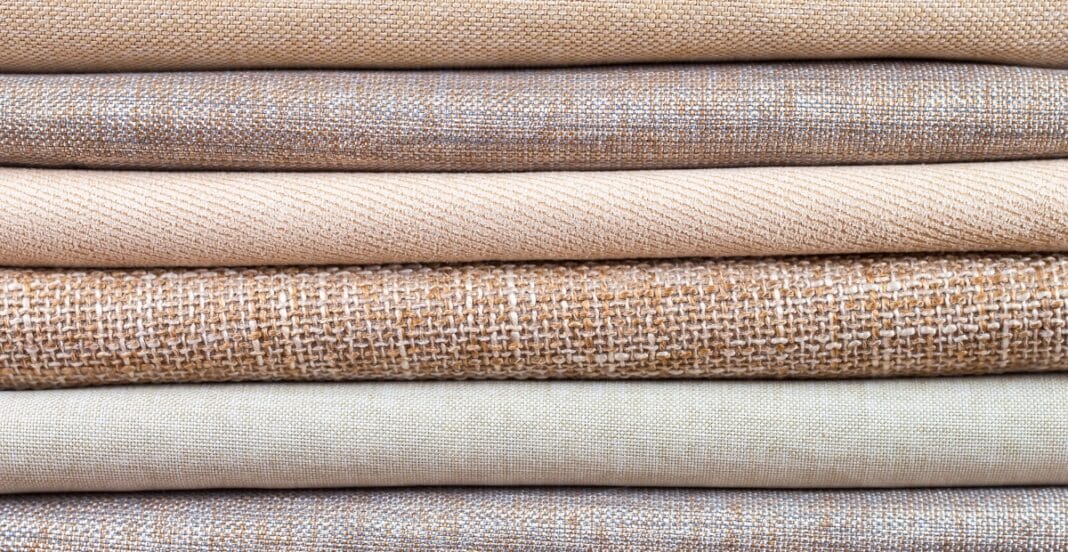 Stack of woven cotton fabrics in various neutral tones with different textures and weaves.