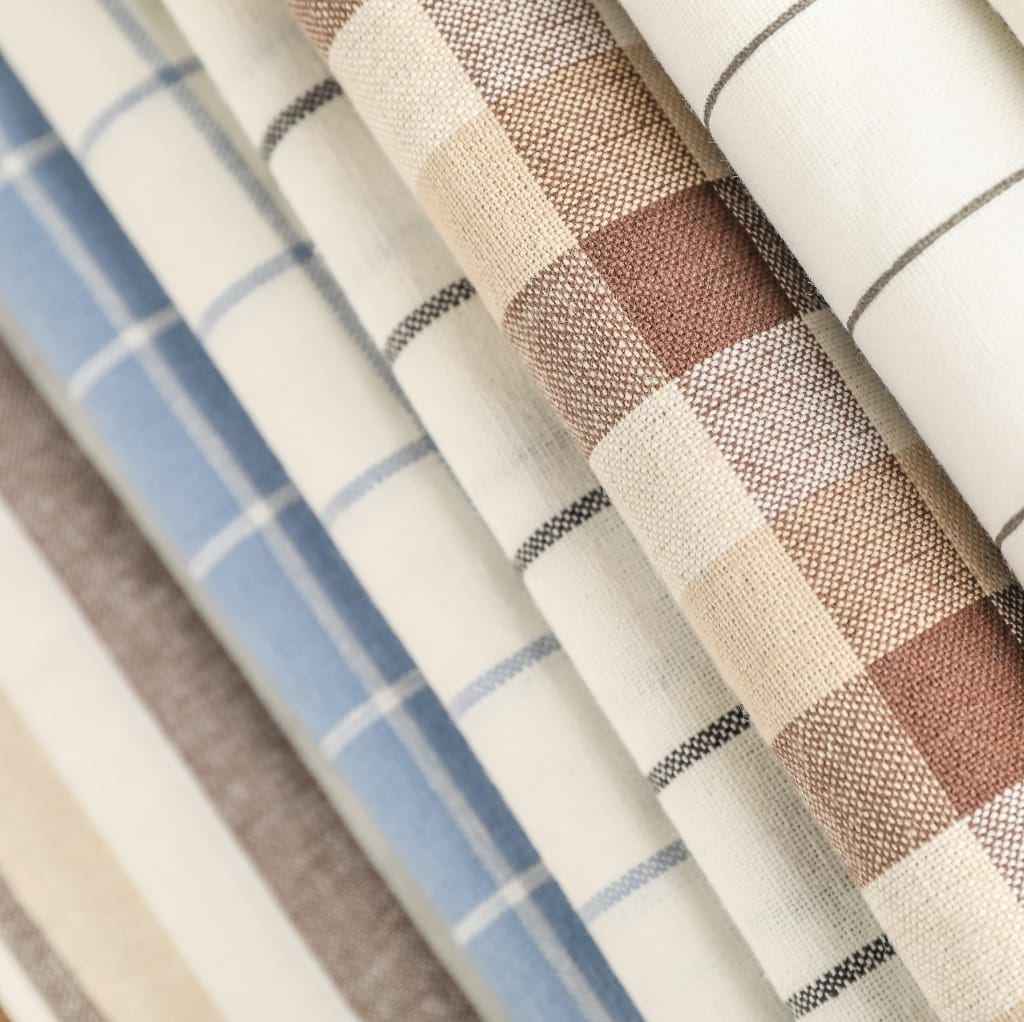 Close-up image of woven cotton fabric in various checked patterns, featuring neutral tones of beige, cream, blue, and brown.