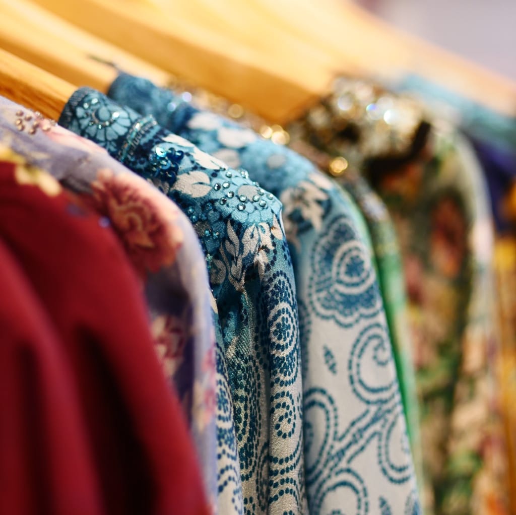 Close-up image of colorful woven cotton garments hanging on a rack, showcasing intricate patterns and designs in various shades.
