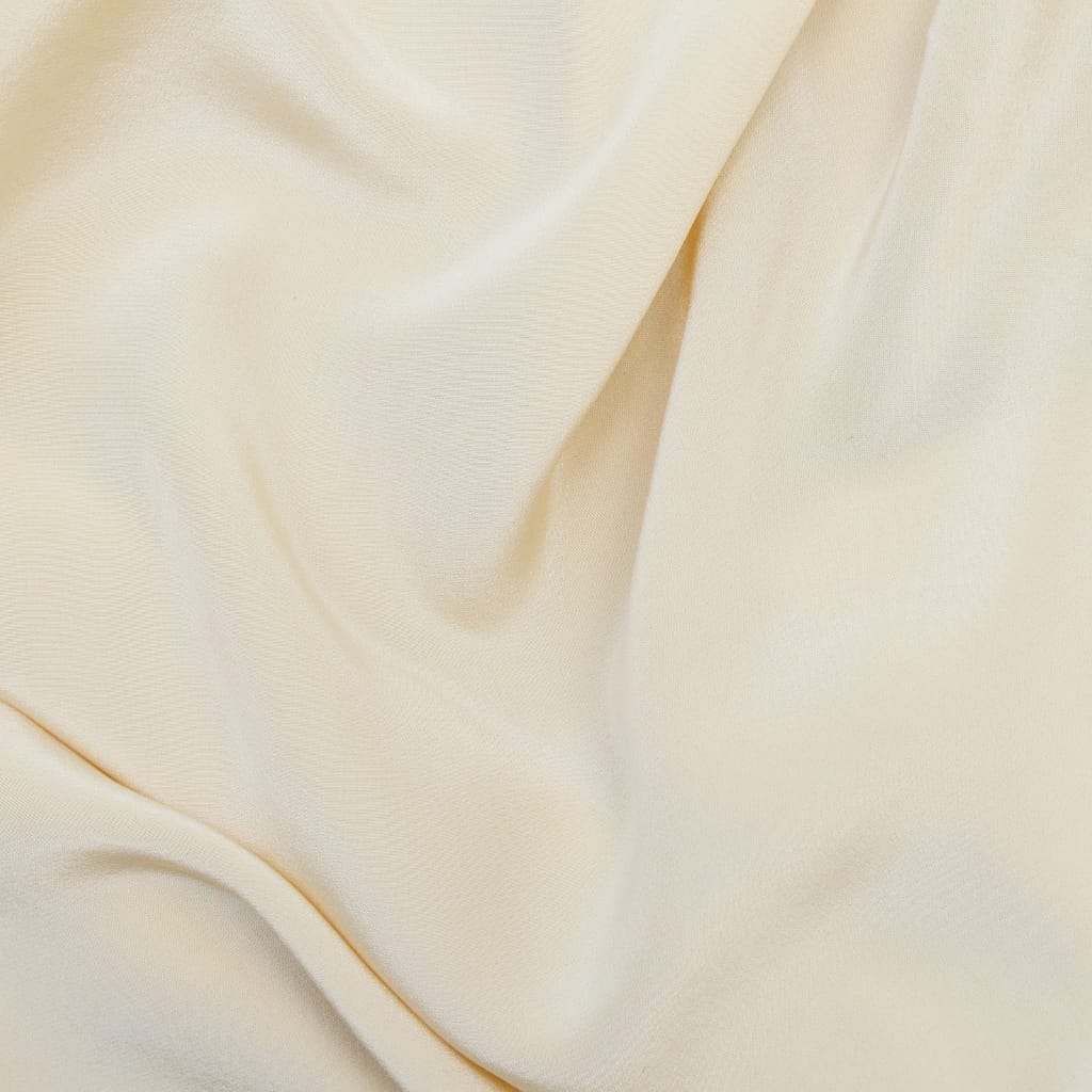 Close-up of smooth, cream-colored fabric with gentle folds, showcasing its soft texture and fine weave.