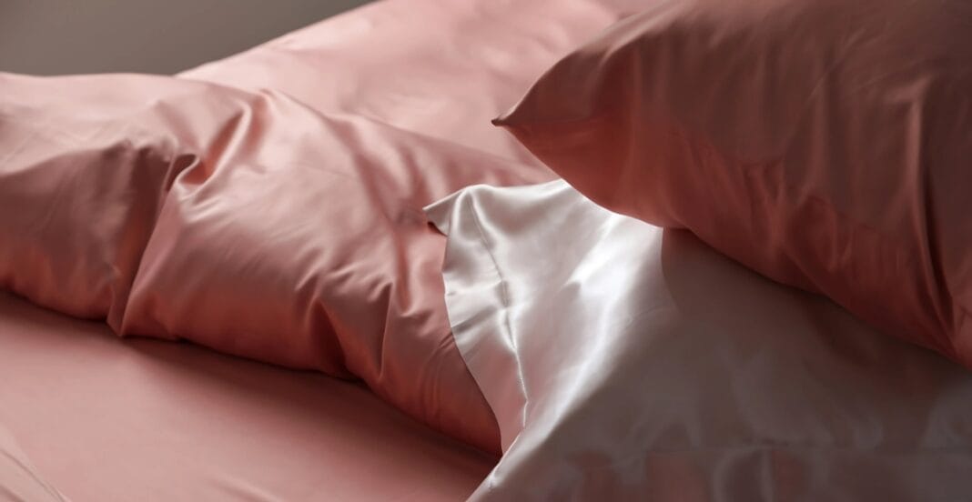 Close-up image of silky pink and white bed sheets and pillowcases with a smooth, shiny texture.
