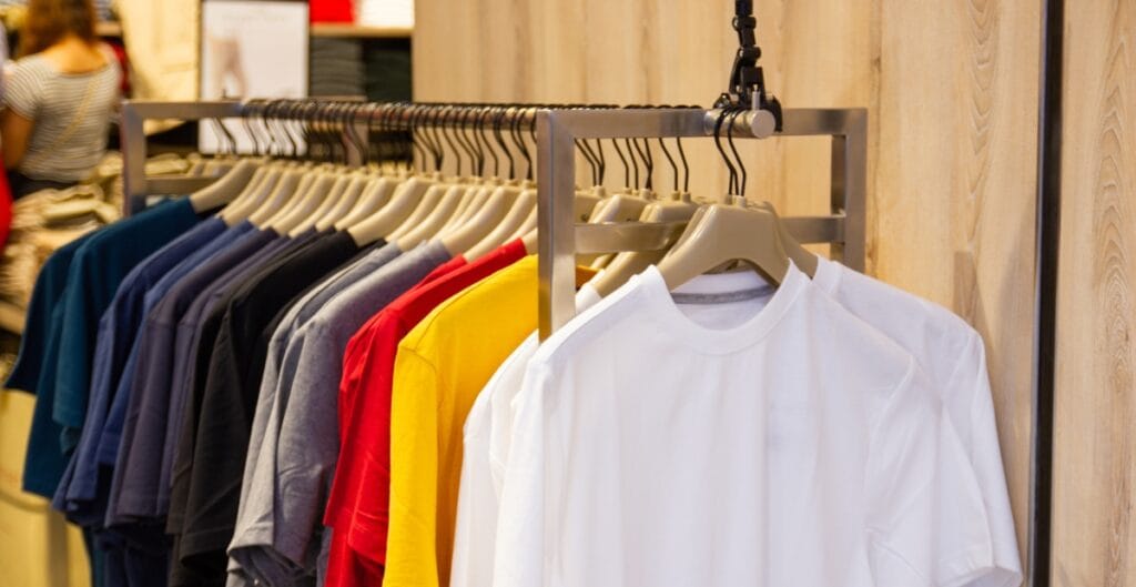 Colorful T-shirts hanging on a rack inside a clothing store, with a white T-shirt prominently in the foreground.