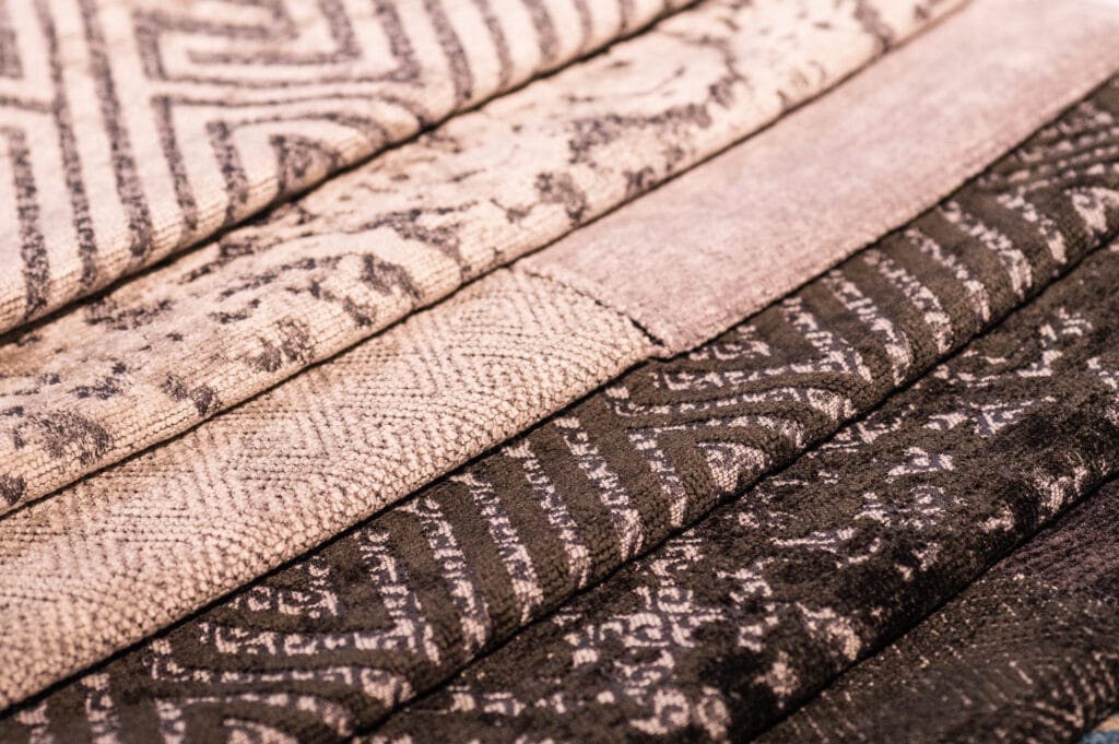 Close-up image of multiple rolls of patterned cotton weaving fabric in shades of beige, pink, and brown.