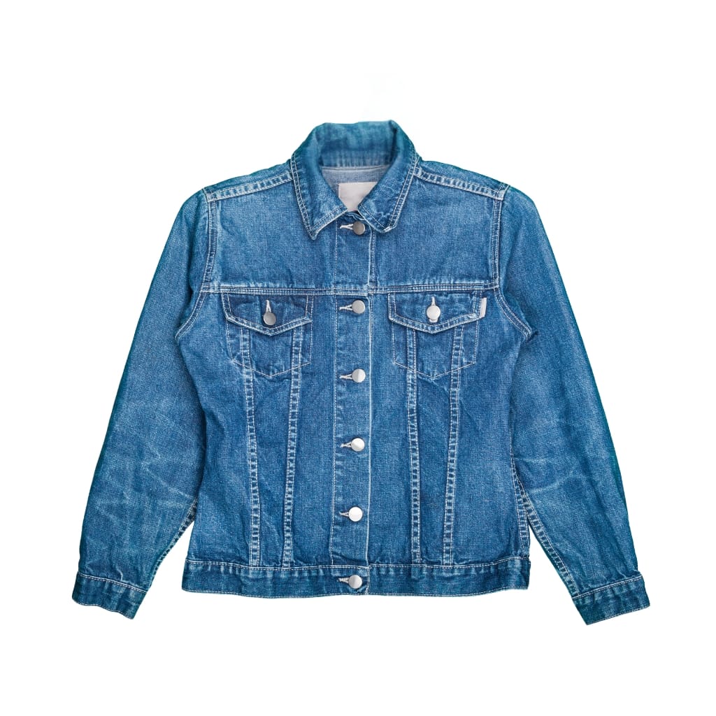 A classic blue chambray denim jacket with front button closure, two chest flap pockets, and buttoned cuffs, shown against a plain white background.