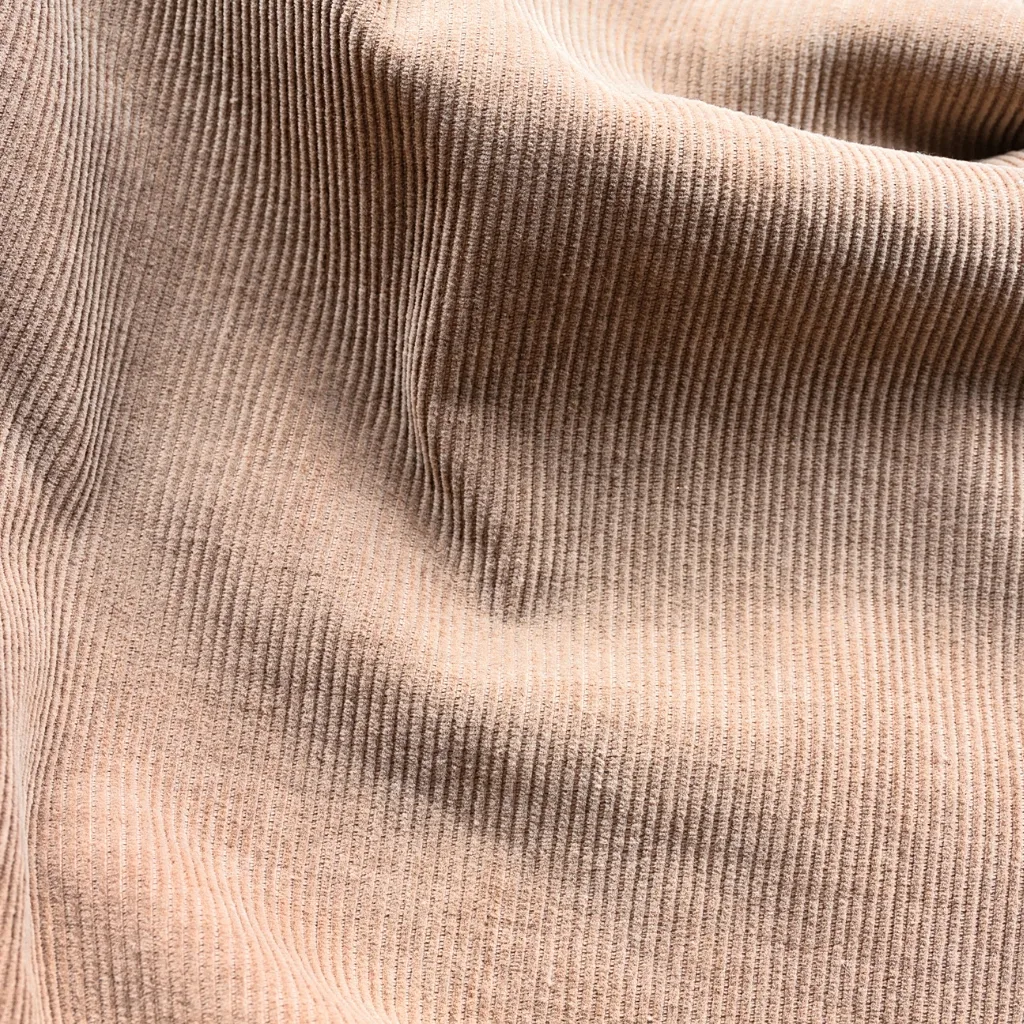 A close-up image of peach-colored corduroy fabric showing its distinctive narrow, parallel ridges (wales) and soft texture.