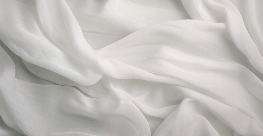 Close-up image of soft, flowing white chiffon fabric with gentle folds and a delicate, lightweight appearance.