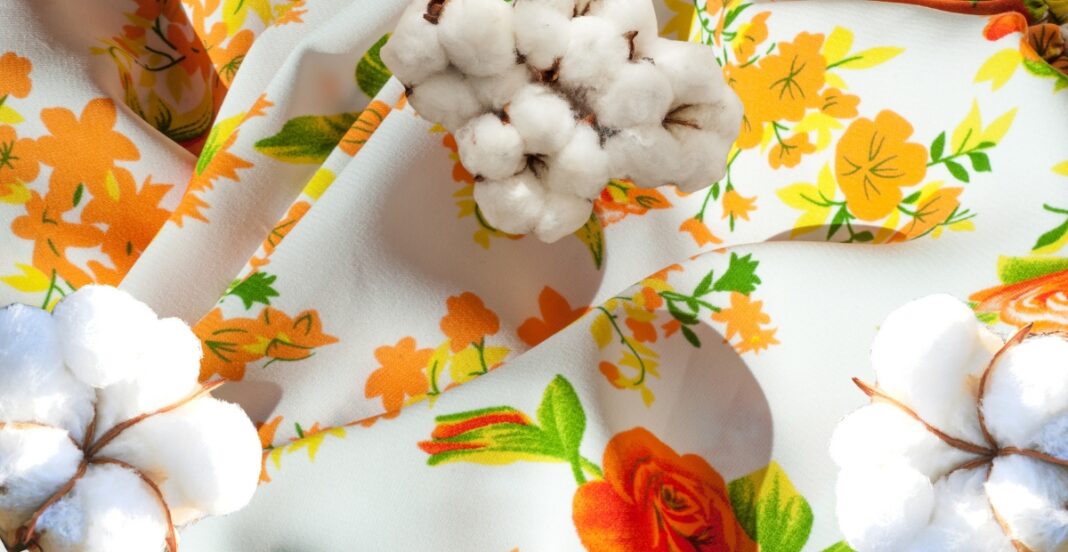 Multicolored floral fabric with orange, yellow, and green patterns, decorated with cotton bolls and a dried cotton stem.