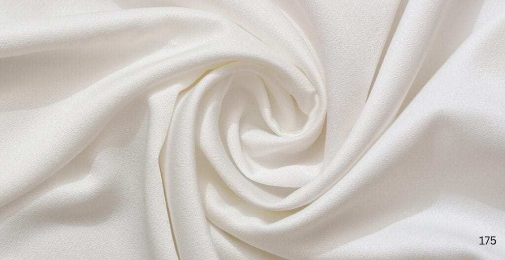 A close-up image of soft, creamy white cotton silk fabric with gentle folds and a smooth, slightly shiny surface.