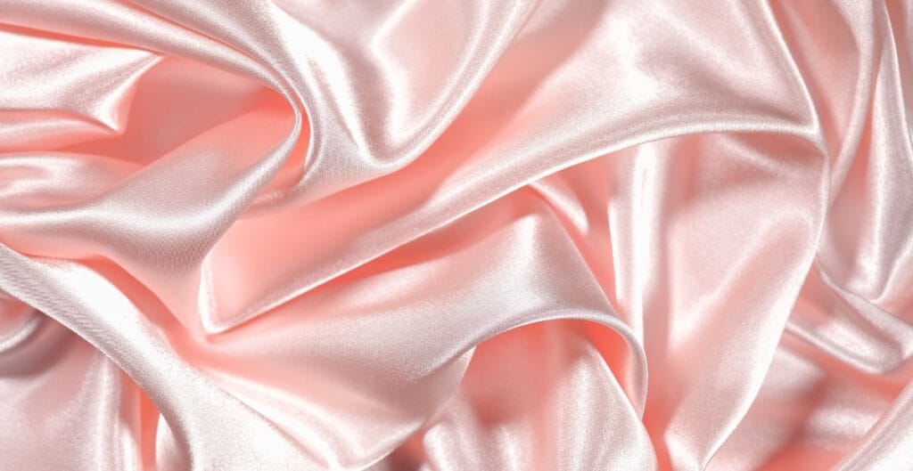 Close-up image of soft, light pink satin-like fabric with smooth, shiny, and slightly wrinkled texture.