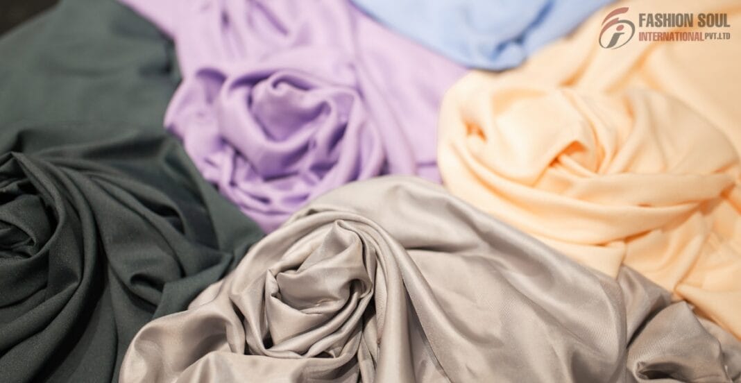 Several pieces of colorful, soft, and shiny fabric in shades of black, purple, cream, peach, and light blue are draped and rolled together on a surface.
