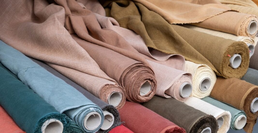: Rolls of fabric in various colors and textures arranged on a table.